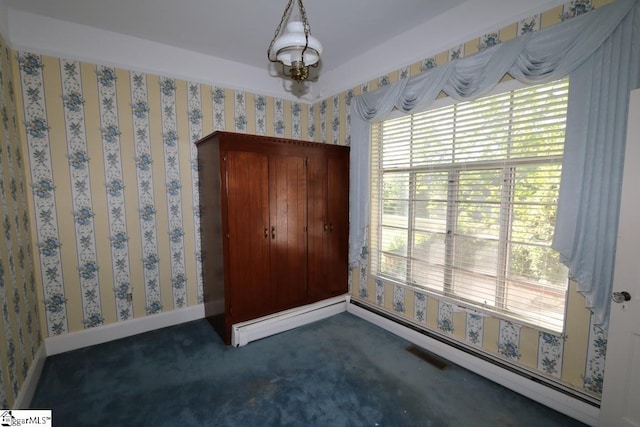 unfurnished room featuring dark carpet, baseboard heating, and a chandelier