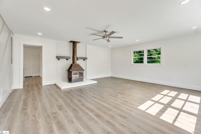 unfurnished living room featuring ceiling fan, a wood stove, and light wood-type flooring