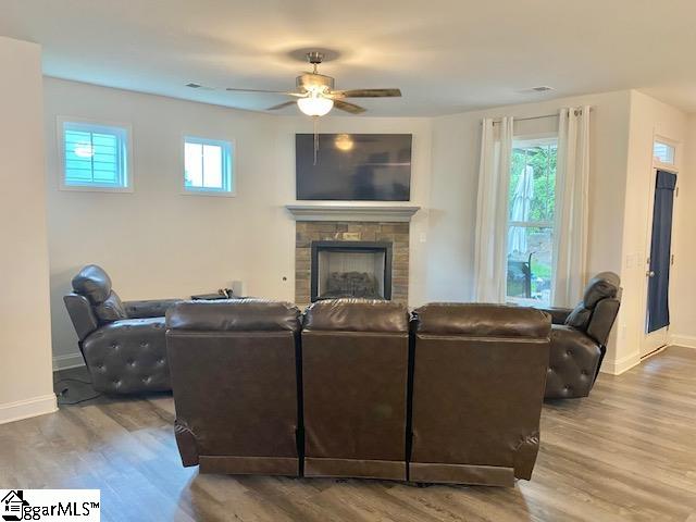 living room with a stone fireplace, hardwood / wood-style flooring, and ceiling fan