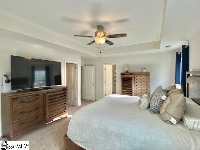 bedroom featuring light carpet, ceiling fan, and a raised ceiling
