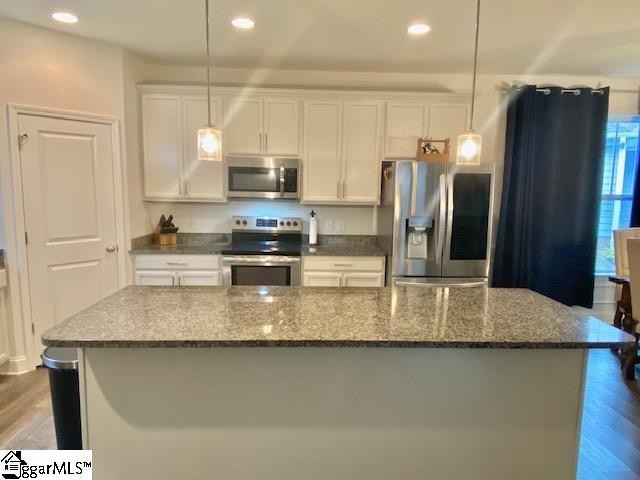 kitchen with hanging light fixtures, wood-type flooring, appliances with stainless steel finishes, and white cabinetry