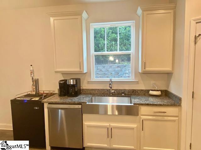 kitchen with dark stone counters, white cabinetry, sink, and stainless steel dishwasher