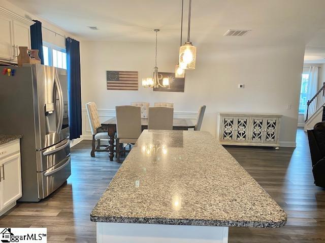 kitchen with a chandelier, dark hardwood / wood-style floors, a kitchen island, stainless steel fridge, and white cabinets