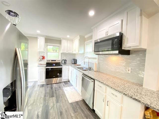 kitchen with tasteful backsplash, light wood-type flooring, white cabinets, sink, and appliances with stainless steel finishes