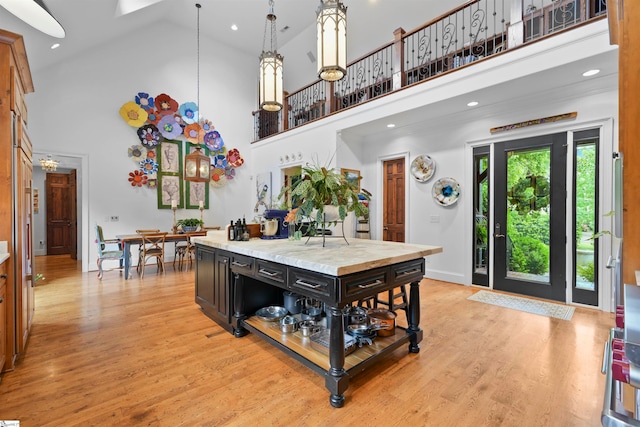 kitchen featuring light stone countertops, decorative light fixtures, light hardwood / wood-style flooring, and high vaulted ceiling