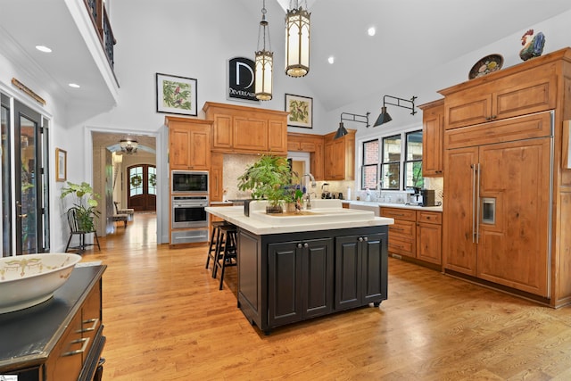 kitchen featuring decorative light fixtures, an island with sink, high vaulted ceiling, and light hardwood / wood-style flooring