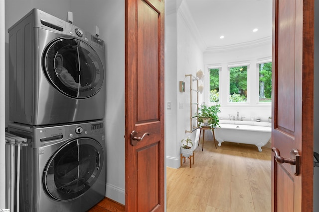 clothes washing area featuring light wood-type flooring, stacked washer and dryer, and crown molding