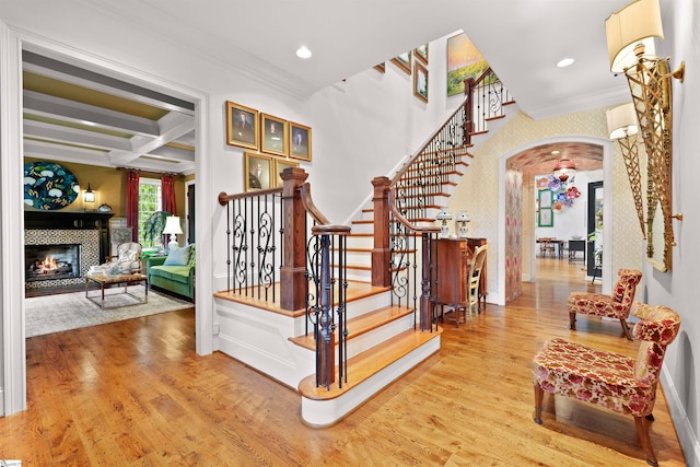 stairway with hardwood / wood-style flooring, crown molding, coffered ceiling, and a tiled fireplace