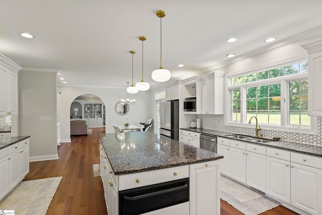 kitchen with arched walkways, a warming drawer, stainless steel appliances, decorative backsplash, and a sink