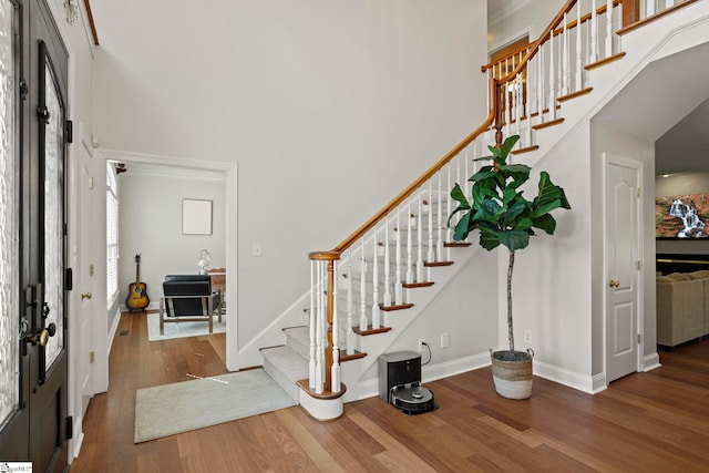 foyer entrance featuring a towering ceiling, stairs, baseboards, and wood finished floors