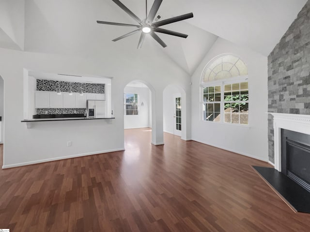 unfurnished living room featuring a stone fireplace, ceiling fan, high vaulted ceiling, and dark hardwood / wood-style floors