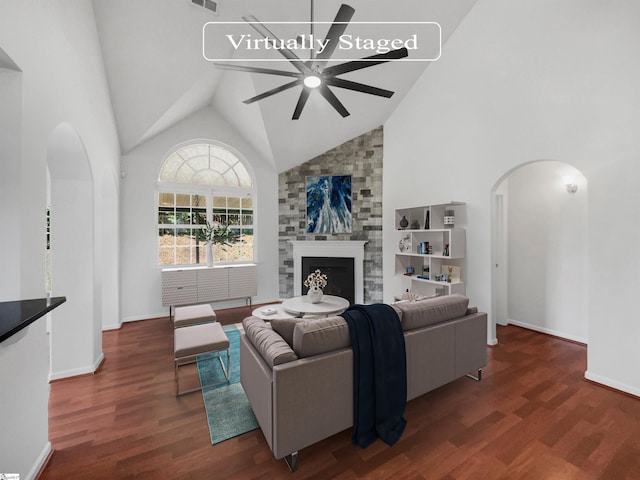 living room with ceiling fan, dark hardwood / wood-style floors, a stone fireplace, and high vaulted ceiling