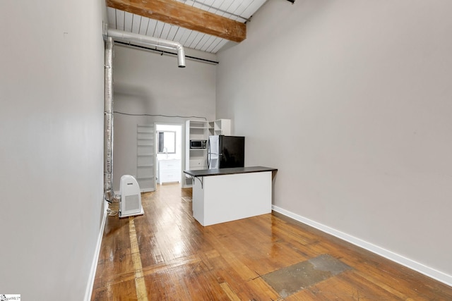 kitchen with hardwood / wood-style floors, wooden ceiling, black fridge, beamed ceiling, and white cabinetry