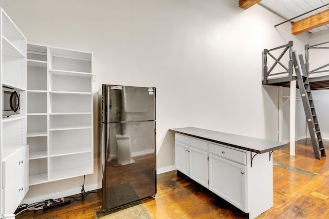 kitchen featuring black refrigerator, kitchen peninsula, a breakfast bar, dark wood-type flooring, and white cabinetry