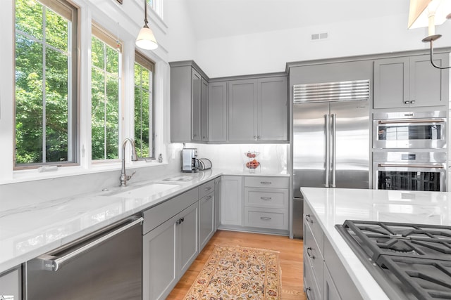 kitchen with light hardwood / wood-style floors, light stone countertops, appliances with stainless steel finishes, gray cabinets, and sink