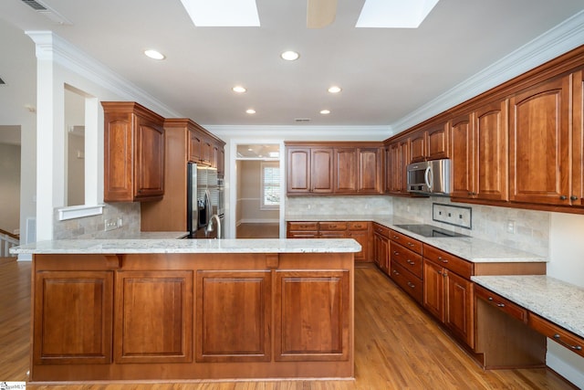 kitchen with kitchen peninsula, appliances with stainless steel finishes, a skylight, and light hardwood / wood-style floors