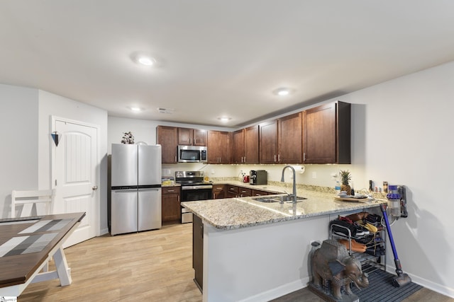 kitchen with sink, light stone counters, kitchen peninsula, stainless steel appliances, and light wood-type flooring