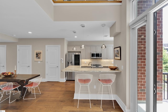 kitchen with hardwood / wood-style floors, a breakfast bar area, decorative backsplash, decorative light fixtures, and stainless steel appliances