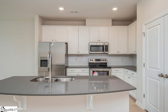 kitchen featuring light hardwood / wood-style flooring, an island with sink, appliances with stainless steel finishes, tasteful backsplash, and white cabinetry