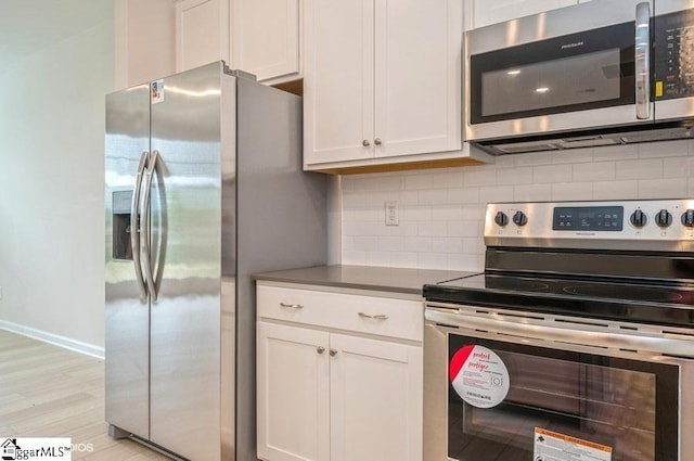 kitchen with white cabinets, decorative backsplash, appliances with stainless steel finishes, and light hardwood / wood-style flooring