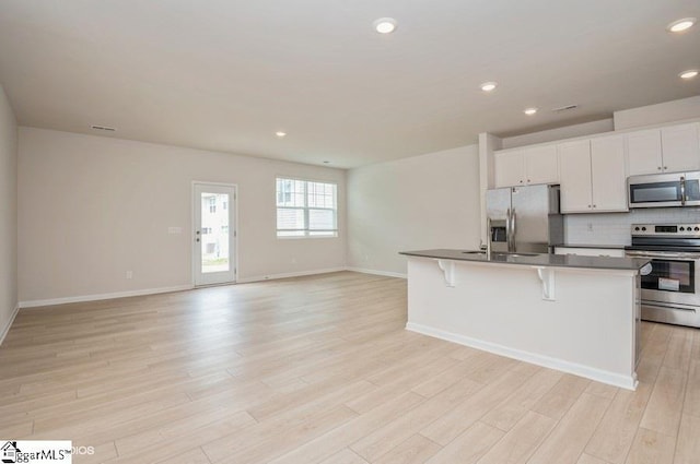 kitchen featuring stainless steel appliances, a center island with sink, light hardwood / wood-style floors, white cabinetry, and a breakfast bar area