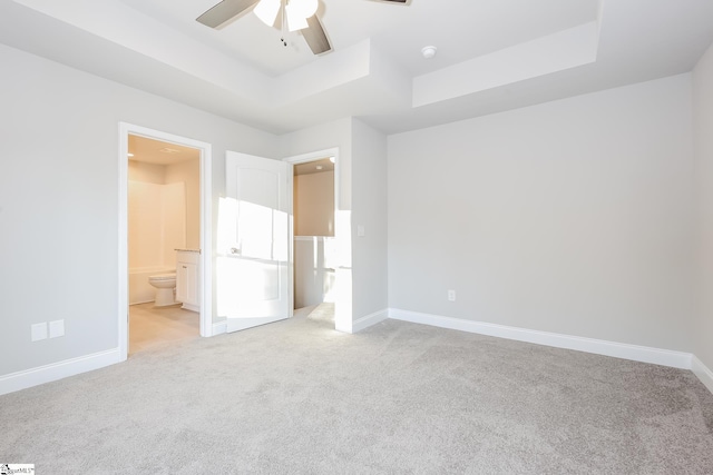 unfurnished bedroom featuring ensuite bathroom, ceiling fan, light carpet, and a tray ceiling