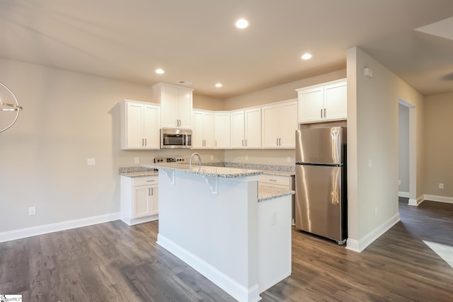 kitchen featuring light stone countertops, appliances with stainless steel finishes, dark wood-type flooring, a center island with sink, and white cabinets