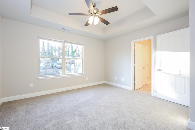 spare room featuring ceiling fan, light colored carpet, and a tray ceiling