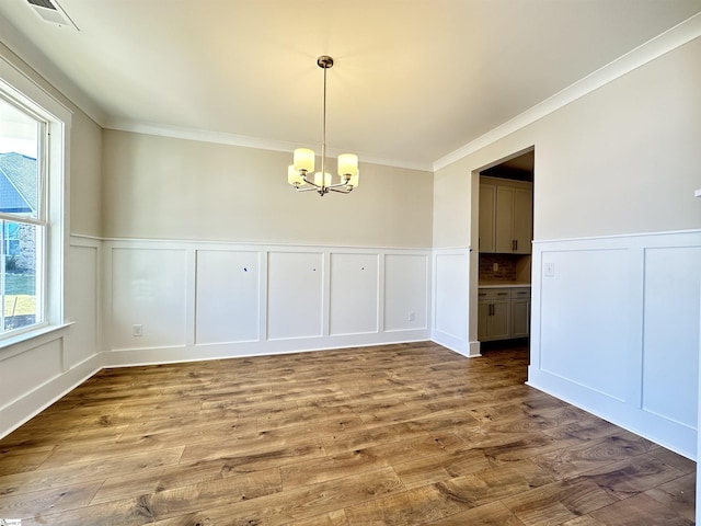 unfurnished dining area featuring hardwood / wood-style floors, crown molding, and an inviting chandelier