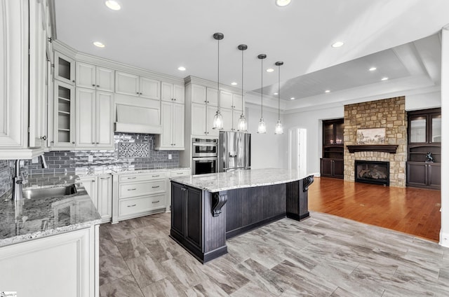 kitchen featuring premium range hood, a center island, white cabinetry, hanging light fixtures, and appliances with stainless steel finishes