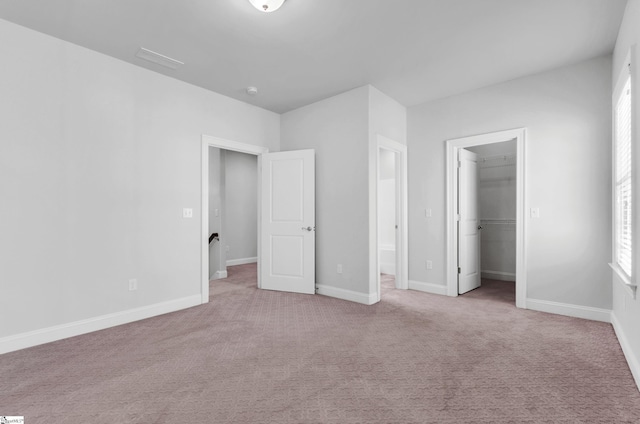 unfurnished bedroom with a spacious closet, a closet, and light carpet