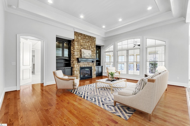 living room with ceiling fan, ornamental molding, a stone fireplace, and light wood-type flooring