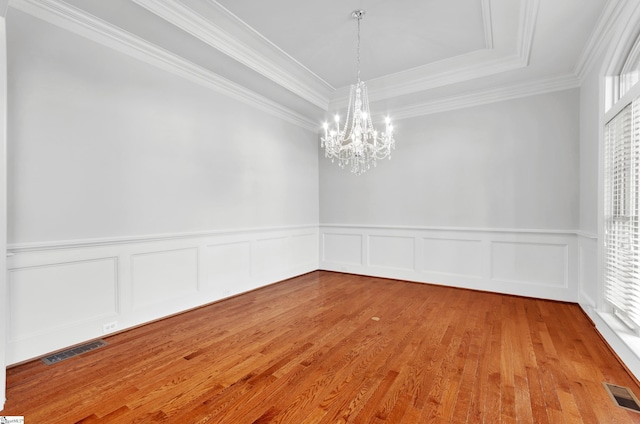 unfurnished room featuring a raised ceiling, a notable chandelier, ornamental molding, and light hardwood / wood-style floors