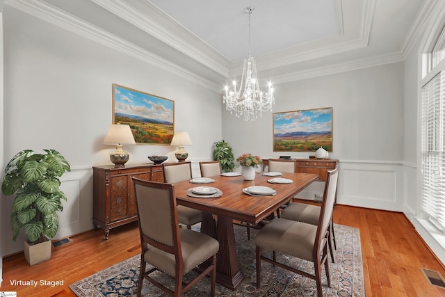 dining space with a tray ceiling, crown molding, a chandelier, and light hardwood / wood-style floors