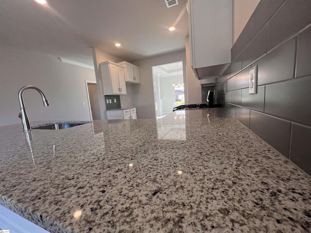 kitchen with recessed lighting, a peninsula, a sink, white cabinets, and light stone countertops