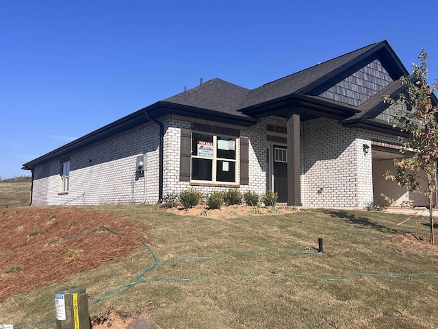 view of side of home featuring a garage, brick siding, a lawn, and a shingled roof