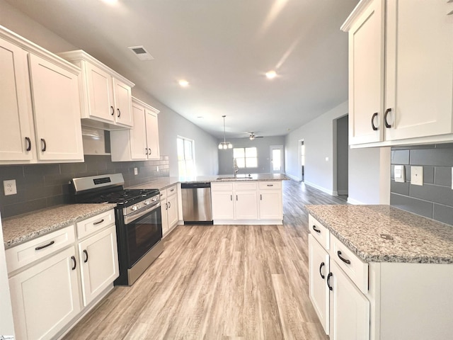 kitchen featuring stainless steel appliances, a peninsula, a sink, light wood-style floors, and backsplash