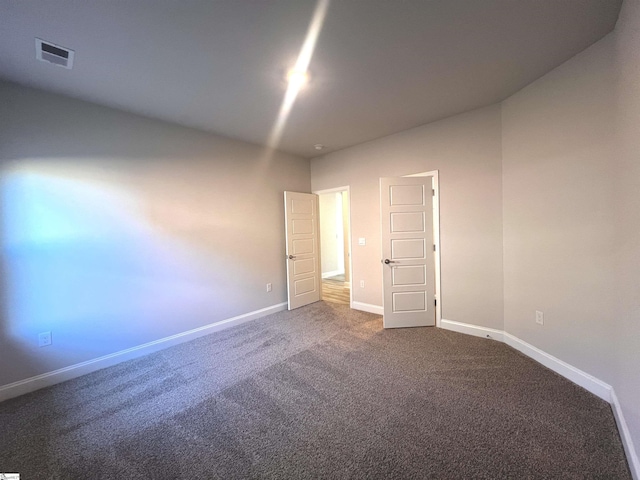 empty room featuring baseboards, visible vents, and dark carpet