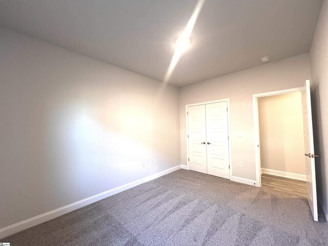 unfurnished bedroom with baseboards, dark carpet, and a closet