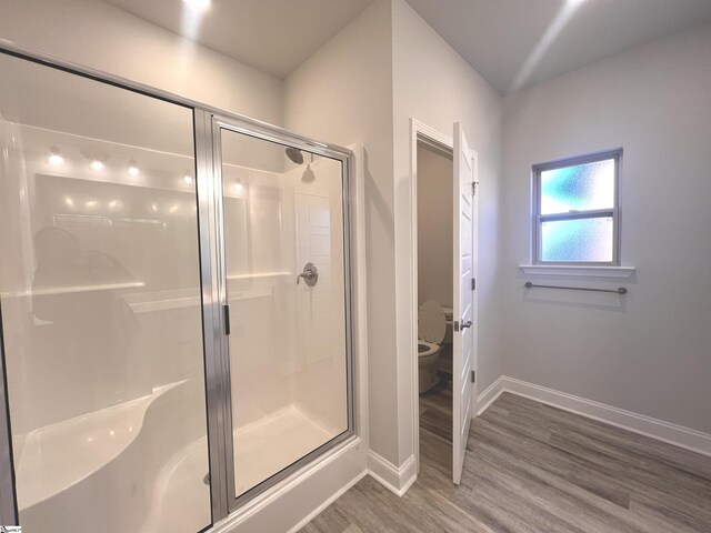 bathroom featuring toilet, a stall shower, baseboards, and wood finished floors