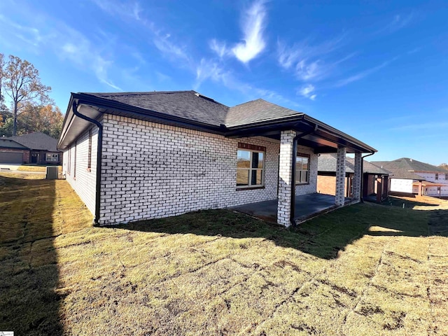 view of side of home with central air condition unit, a lawn, a patio, and brick siding