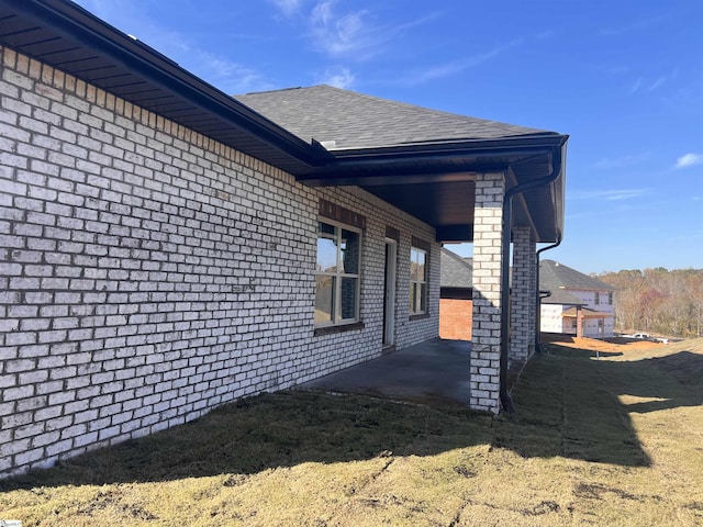 view of home's exterior featuring a patio area, a shingled roof, and brick siding