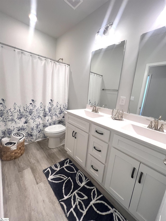 full bathroom featuring toilet, double vanity, a sink, and wood finished floors