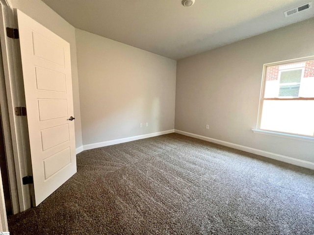 spare room featuring dark colored carpet, visible vents, and baseboards