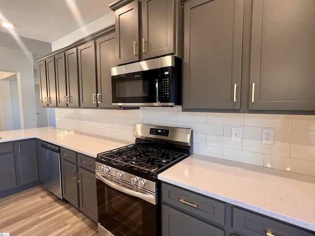 kitchen with appliances with stainless steel finishes, light hardwood / wood-style floors, tasteful backsplash, and light stone counters