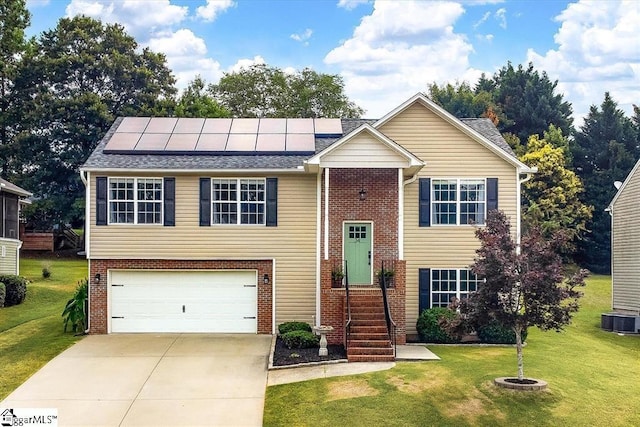 bi-level home featuring solar panels, cooling unit, a front yard, and a garage