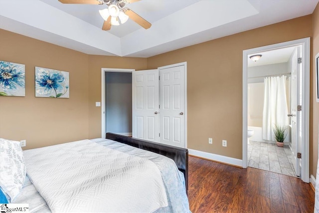 bedroom with ceiling fan, dark wood-type flooring, a raised ceiling, ensuite bathroom, and a closet