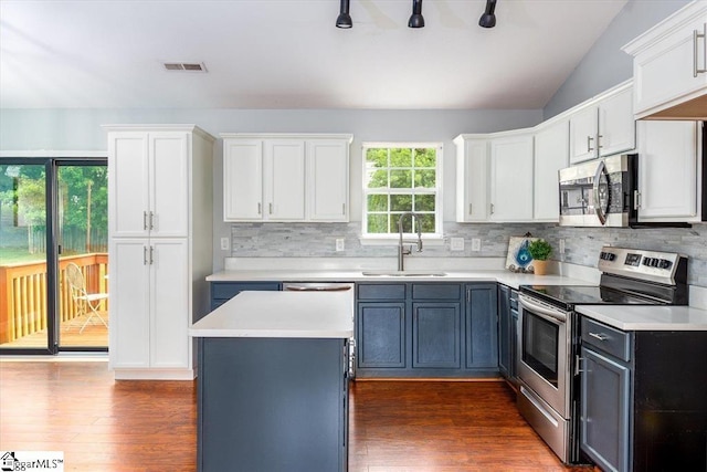 kitchen with lofted ceiling, backsplash, white cabinets, sink, and appliances with stainless steel finishes