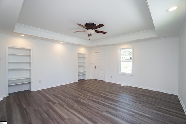 unfurnished room with built in shelves, ceiling fan, dark wood-type flooring, a raised ceiling, and ornamental molding