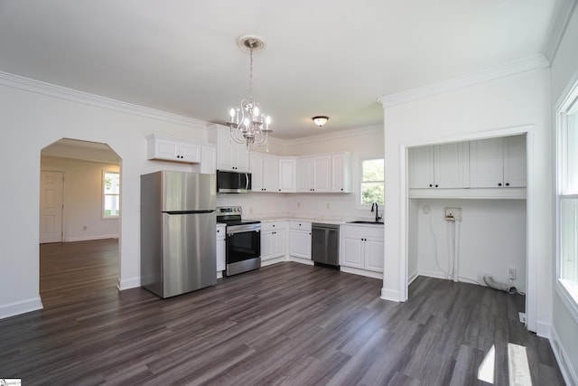 kitchen with appliances with stainless steel finishes, ornamental molding, dark wood-type flooring, white cabinets, and hanging light fixtures